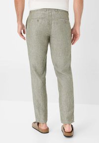 Light green linen trousers with a textured surface, tapered legs, elastic waistband, and two back pockets featuring button closures.
