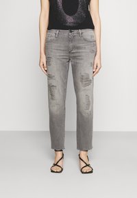 Jeans grises desgastados con dobladillo deshilachado, con rasgaduras y un corte relajado. Combinados con una camiseta negra con estampado de lentejuelas y sandalias de tiras.