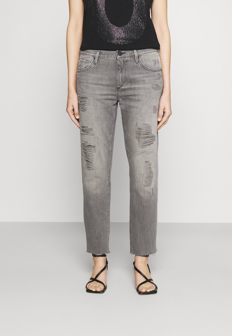 Jeans grises desgastados con dobladillo deshilachado, con rasgaduras y un corte relajado. Combinados con una camiseta negra con estampado de lentejuelas y sandalias de tiras.