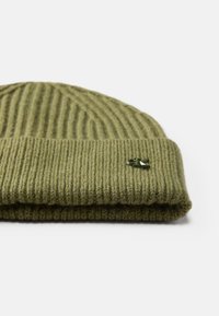 Gorro de malha verde-oliva com textura canelada e design com dobra. Apresenta um pequeno detalhe decorativo escuro na frente.