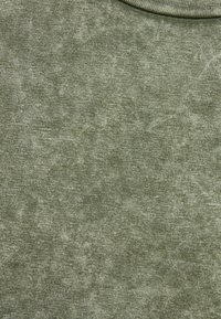 Olivgrön tyg med en texturerad yta, som har ett subtilt, ojämnt mönster och fin ribbning. Cirkulär halsringning, mjukt och lätt material.