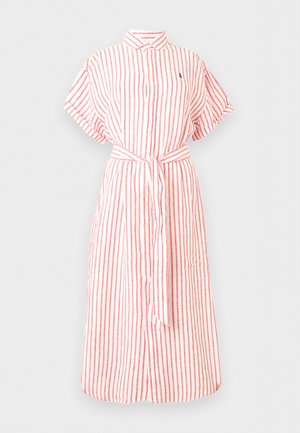 Femme portant une robe rose et blanche à rayures, longueur genoux, manches courtes, avec un lien à la taille, portant un sac à épaule blanc et des sandales marron à lacets.