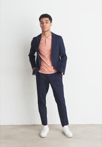 Granatowa marynarka i spodnie w połączeniu z jasnoróżową koszulką polo i białymi sneakersami. Gładki materiał z dopasowanym krojem. Minimalistyczny design.