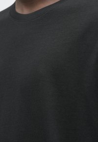 Ingrandimento di una persona che indossa una t-shirt a girocollo grigio scuro semplice, che mostra la parte superiore del torace e la zona del collo.