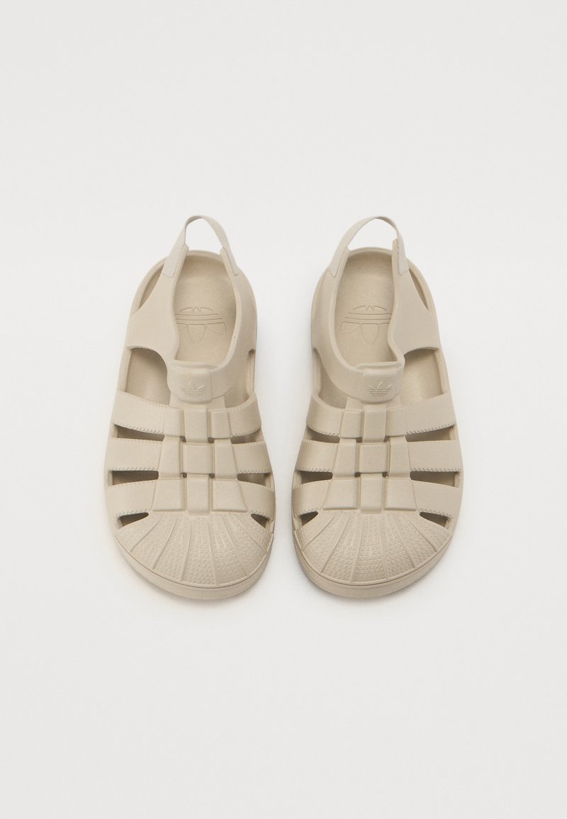 Beige Kunststoffsandalen mit geschlossener Zehenpartie, offenen Seiten und einem hinteren Fersenriemen. Mit horizontalen und vertikalen Ausschnitten für Belüftung.