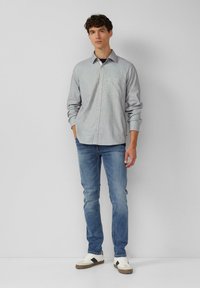 Lichtgrijze overhemden met een subtiel ruitpatroon, met lange mouwen en een borstzak, gecombineerd met blauwe jeans en witte sneakers.