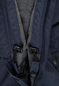 Interior de la chaqueta navy con forro de forro polar gris, cremallera y cordones ajustables; presenta una tela lisa y elegante y herrajes funcionales.