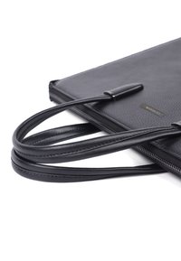 Sort tekstureret læder tote bag med glatte hanke, med lynlås lukning og et lille, diskret mærkeskilt på siden.