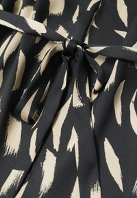 Tissu noir avec un motif de coups de pinceau crème, doté d'une fermeture à ceinture nouée. Texture lisse, design semi-structuré et drapé doux.