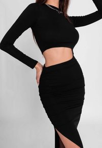 Musta lyhythihainen crop-top, yhdistettynä rypytettyyn mustaan maxihameeseen, jossa on sivureikä ja sileä rakenne. Hopeinen kaulakoru korostaa asua.