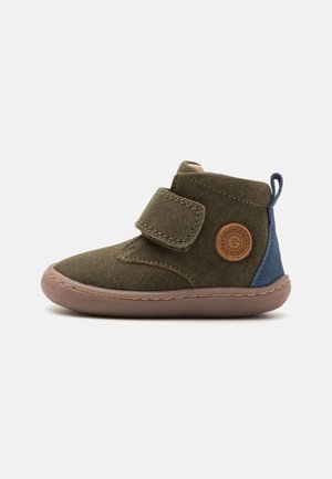 Stivaletto in camoscio verde con un accento blu, due cinturini in Velcro, punta rotonda e suola in gomma. Presenta un logo circolare sul lato.