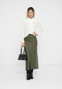 White ruffled blouse, olive green fitted skirt, black handbag, and knee-high black boots. Smooth fabric, sleek design, and tailored fit.