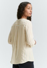 Cremefarvet og beige stribet blouse med trekvartærmer, letvægtsstof, afrundet kant og rygfold.