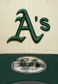 Czapka w kremowym kolorze z zielonym haftowanym logo "A's", regulowany tył i dopasowany daszek. Na daszku znajduje się naklejka z logo New Era 9FORTY.