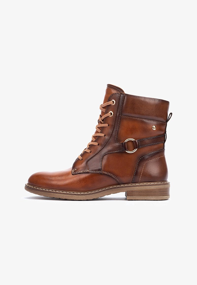 Brown leather ankle boot with lace-up front, decorative metal ring detail on side, low heel, and contrasting stitching along the sole edge.
