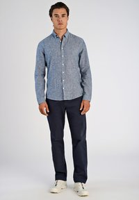 Camisa de cuadros azul con botones, pantalones oscuros de color marino y zapatillas blancas. La camisa tiene un cuello estructurado y está hecha de una tela texturada.