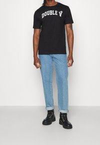 Černé tričko s tučným bílým textem "DOUBLE", v kombinaci se světle modrými džíny rovného střihu a černými šněrovacími botami.