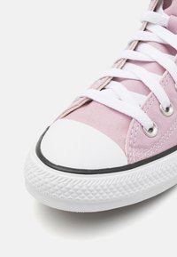 Rosa canvas-sneakers med vit gummitå och vita snörningar, samt silverfärgade öglor. Har texturerad sula och svart kant längs sulan.