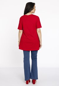 Rode tuniek met korte mouwen en een ronde halslijn, gecombineerd met blauwe flared jeans en rode hakken. Glad materiaal met een losse pasvorm.