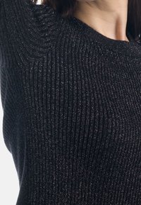 Sweater noir à côtes avec des accents de fil métallique, col rond, forme ajustée et tissu texturé.