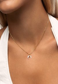 Gouden ketting met een kleine witte maansikkel pendant, met een soepele textuur en een minimalistisch ontwerp.