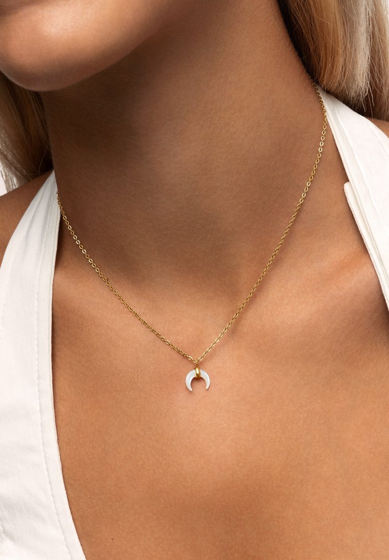 Gouden ketting met een kleine witte maansikkel pendant, met een soepele textuur en een minimalistisch ontwerp.