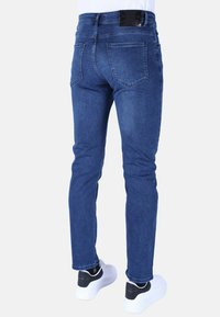 Blauwe spijkerbroek met een slim fit ontwerp, vijf zakken en een zwart leren merklabel op de tailleband. Draag met witte sneakers.