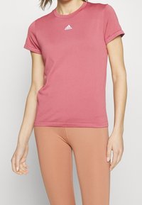 Rosa tränings t-shirt med korta ärmar, rund hals och Adidas-logotyp på bröstet. Slätt, stretchigt material med en tight passform.
