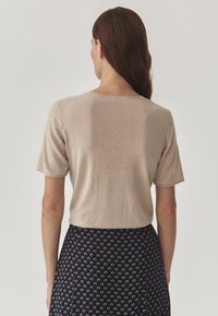 Haut beige à manches courtes avec un col rond, présenté avec une texture lisse, associé à une jupe foncée à motifs affichant de petits dessins de fleurs.