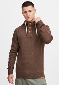 Sudadera marrón de cuello redondo hecha de una tela suave con un bolsillo tipo canguro. Cuenta con un cuello abotonado y cordones de color crema. Etiqueta de marca sutil en el lateral.