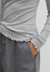 Ljusgrå ribbad långärmad skjorta med en scalloperad fåll och manschetter, i kombination med mörkgrå byxor som har en mjuk textur.