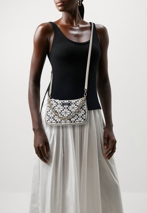 White and navy floral patterned shoulder bag with a curved shape, chain strap, and textured fabric; worn over a black top and white skirt.