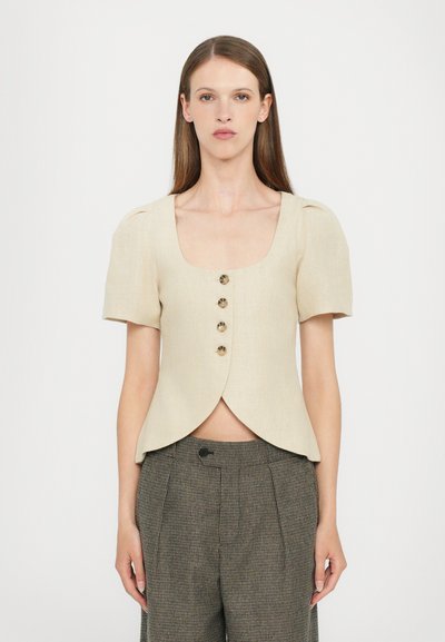 Blusa de lino crema de manga corta con escote cuadrado y seis botones marrones. El diseño cuenta con un dobladillo con forma de picos y hombros estructurados.