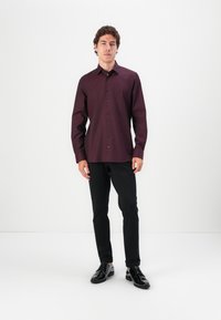 Weinrot langärmeliges Hemd mit Knopfverschluss vorne, schwarzen Knöpfen, kombiniert mit schwarzen Slim-Fit-Hosen und glänzenden schwarzen Schuhen.