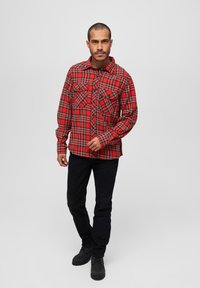 Rødternet flannel skjorte med to frontlommer og knaplukning, parret med sorte jeans og sorte støvler. Glat stoftekstur.