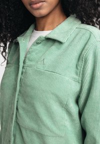 Light green corduroy button-up with a collared neck, ribbed texture, and subtle embroidery detail on the chest. Buttons are a matching hue.