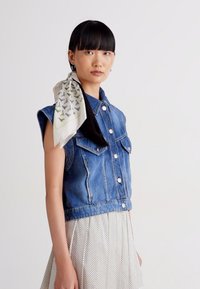 Denim vest with a cropped design, buttoned front, and two chest pockets; paired with a light polka dot skirt and a patterned silk scarf.