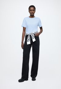 Ανοιχτό μπλε κοντομάνικο μπλουζάκι συνδυασμένο με μαύρο παντελόνι φαρδιάς γραμμής. Λευκό και μαύρο ριγέ πουλόβερ δεμένο στη μέση. Μαύρα μποτάκια.