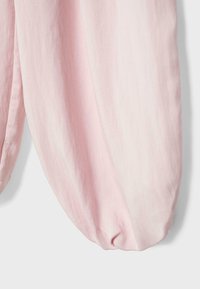 Mehka roza tkanina, razpeta v ohlapne gube z zaobljenim, nabranim robom na enostavni svetli podlagi.