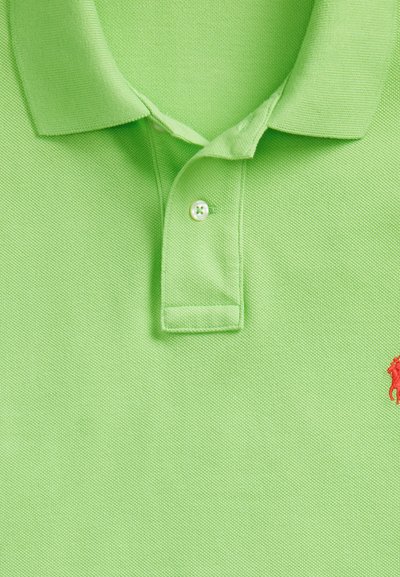 Svijetlozelena polo majica s preklopljenim ovratnikom, jednim bijelim zakopčanim gumbom i malim crvenim izvezenim logotipom na desnoj strani.