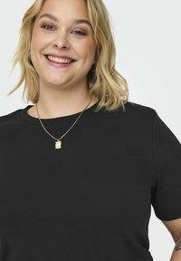 T-shirt preto de manga curta com decote redondo, feito de tecido de algodão suave. Um colar dourado com um pingente é usado ao redor do pescoço.