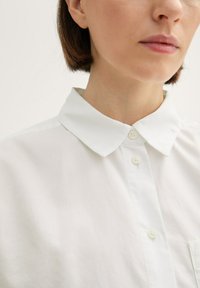 Weißes Rollkragenhemd mit einer geknöpften Leiste, aus glattem Stoff gefertigt. Verfügt über eine kleine Tasche auf der Vorderseite und ein klassisches Kragen-Design.