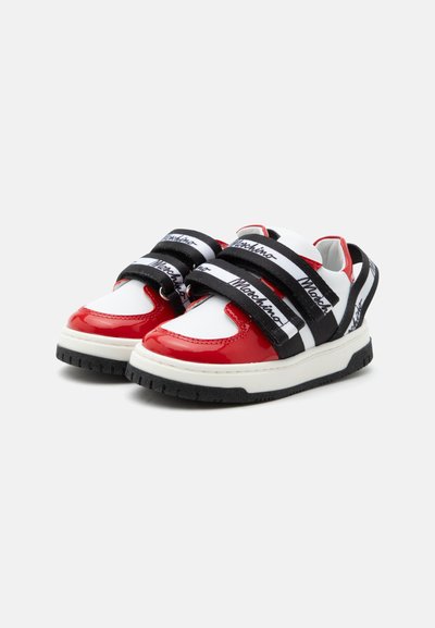 Άσπρα και κόκκινα sneakers με μαύρες και άσπρες λουρίδες Moschino και χοντρές λευκές σόλες, τοποθετημένα σε γωνία για να δείξουν μπροστινή και πλευρική όψη.