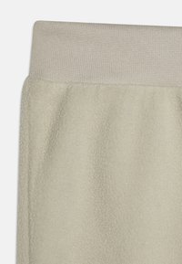 Light beige fleece joggers with a textured, ribbed waistband. The fabric is soft and slightly fluffy, providing a cozy appearance.