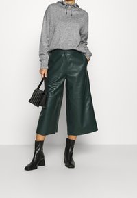 Felpa grigia con cappuccio e cordini, abbinata a culotte in pelle verde scuro e stivaletti neri con tacco. Borsa a tracolla nera e trapuntata in mano.