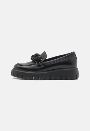 Black leather loafer with a chunky rubber sole, decorative knotted detail on the vamp, and smooth texture. Sleek, low-cut design.
