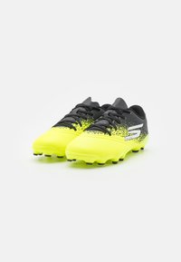 Botas de fútbol negras y amarillo neón con una parte superior texturizada, diseño degradado y tacos negros para tracción. Cuenta con cierre de cordones.