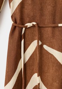 Tissu marron avec des motifs abstraits blancs, muni d'une ceinture étroite nouée d'un simple nœud autour de la taille.