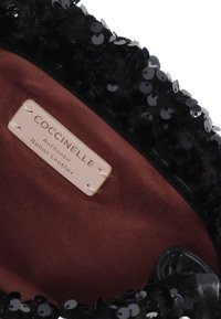 Interno di una borsa nera con paillettes, foderato in tessuto marrone. Presenta un'etichetta con la scritta "Coccinelle Authentic Italian Leather" attaccata con cuciture.
