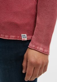 Rotes Waffelstrick Langarmshirt mit abgerundetem Saum und geknöpften Ärmeln. Zeigt ein Etikett mit "CAMP DAVID" in der Nähe des unteren Saums.